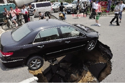 A car stuck above a sinkhole that formed underneath the road.