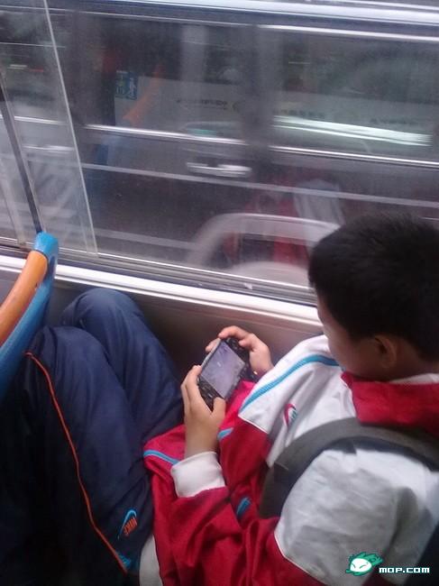 A young Chinese schoolboy plays with his PSP on his bus ride home.