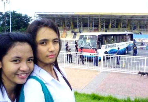 Two Filipino schoolgirls taking photos in front of the Hong Thai Travel tour bus where Hong Kong tourists were held hostage and killed.