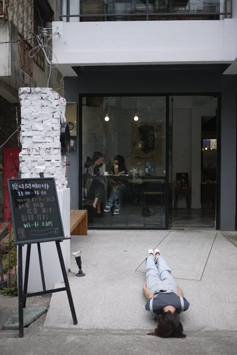 In Taiwan, a girl lies flat on the ground outside a small cafe restaurant.