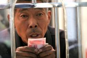Elderly Chinese man holding 100 RMB bill preparing to purchase a train ticket.