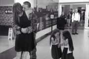 Two little girls giggle as a soldier kisses his wife after reuniting at the airport.